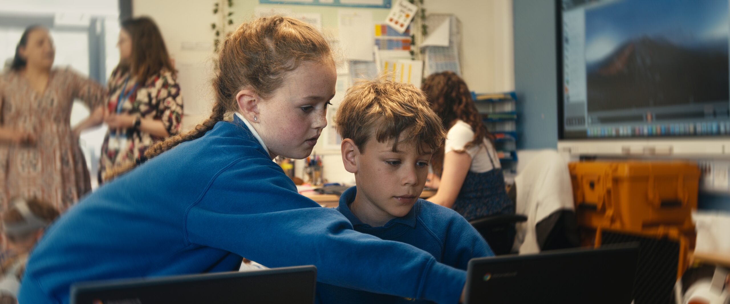 A girl showing a boy something on a computer